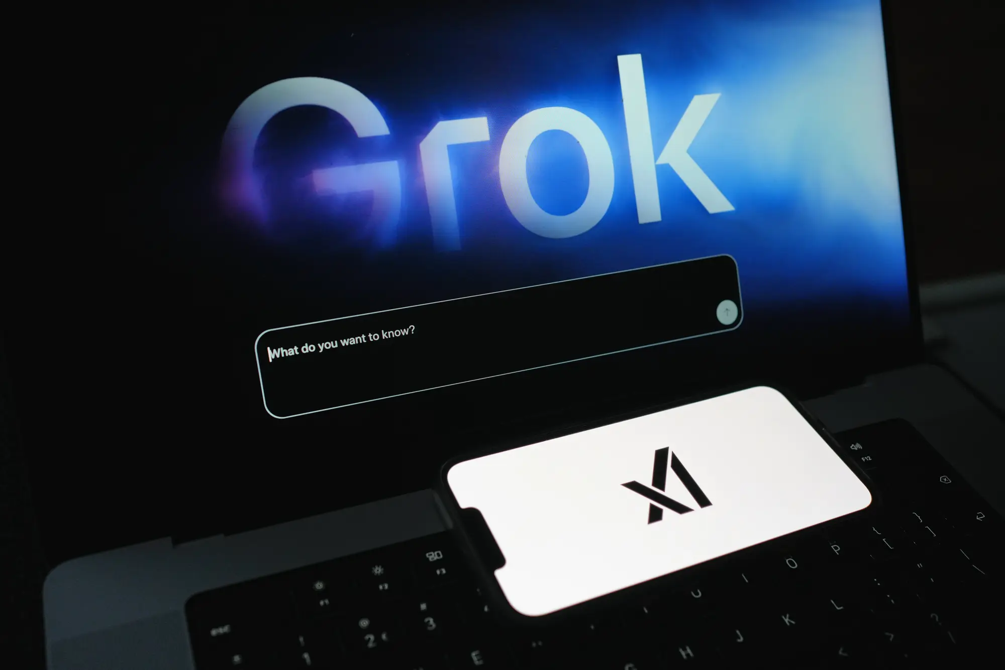 Grok AI Chats welcome screen on laptop with Grok logo on mobile phone